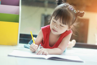 Girl writing in book while lying on floor