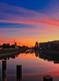 Buildings by river against sky during sunset