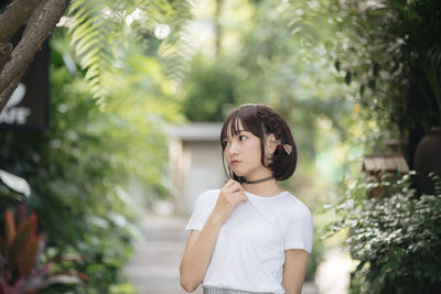 Young woman looking down while standing against trees