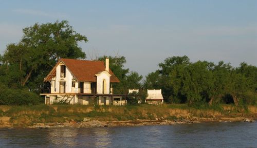 House and trees by lake against sky