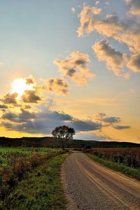 Dirt road on field against sky during sunset