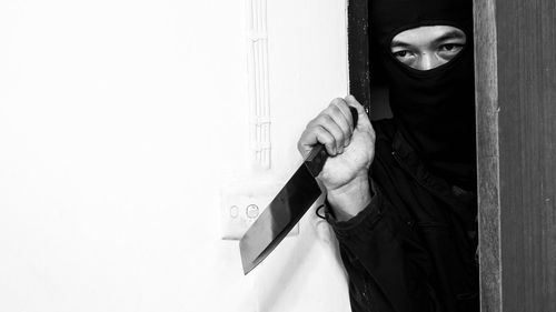 Portrait of person wearing mask standing against white wall