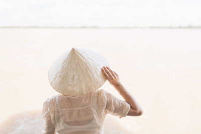 Rear view of woman wearing asian style conical hat at beach