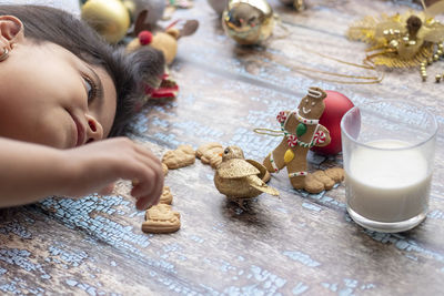 Close-up of girl lying down by baked cookies on wooden flooring