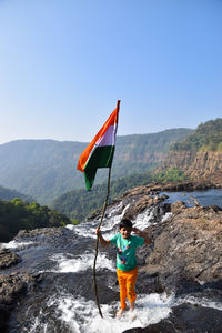 Boy standing on rock against mountain against clear sky with indian flag