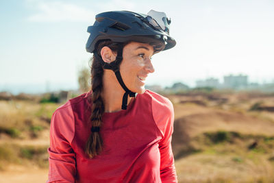 Sportswoman in black helmet and red sportswear with glasses resting near training track looking away