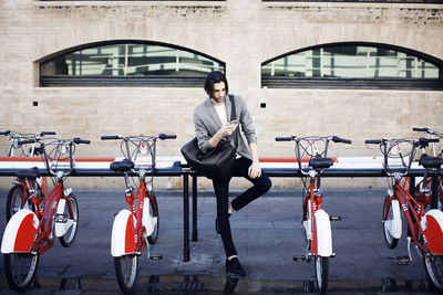 Man with bag using mobile phone while standing at bicycle parking station