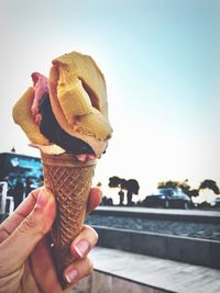 Cropped hand of woman holding ice cream cone against sky