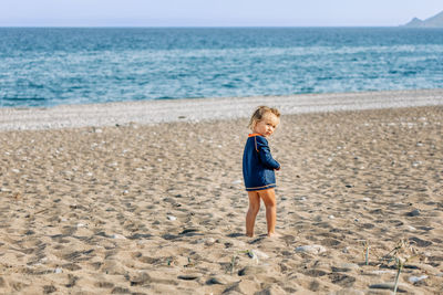 Side view of cute baby girl standing at beach during sunny day