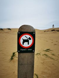 Close-up of sign on wooden post at beach against sky