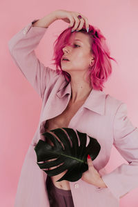 Young woman with dyed hair holding leaf while standing against colored background