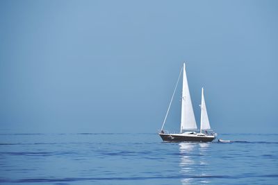 Sailboat sailing in sea against clear blue sky