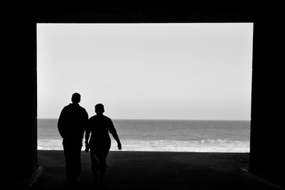 Silhouette men standing on beach against clear sky