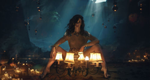 Full length portrait of woman sitting by illuminated lighting equipment in darkroom