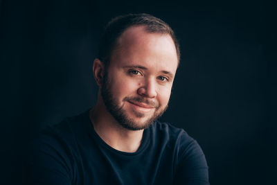 Close-up portrait of smiling young man against black background