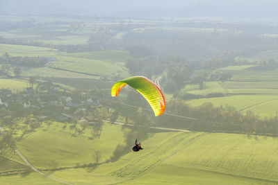 Person paragliding over green landscape