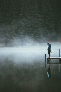 Reflection of man on lake against trees during foggy weather