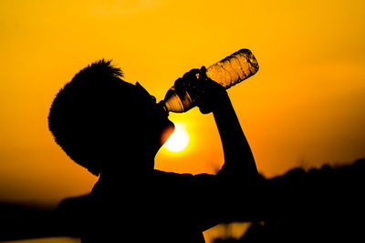 Silhouette boy drinking water against sky during sunset