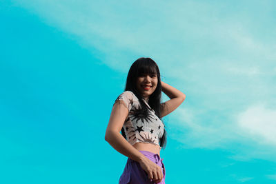 Portrait of young woman standing against blue sky
