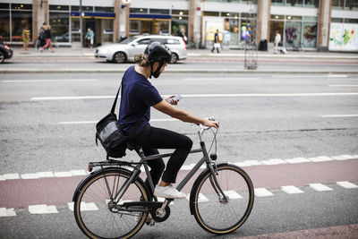 Full length of man using phone while cycling on city street