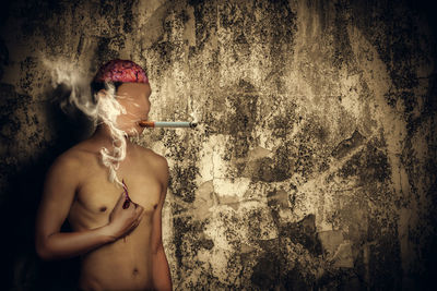 Young woman smoking cigarette against wall