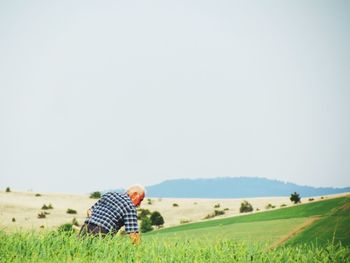 Rear view of senior man working on agricultural field against clear sky