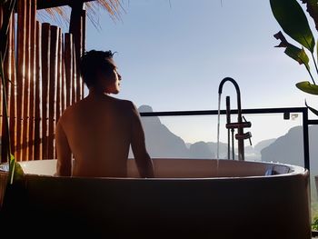 Rear view of shirtless man bathing in bathtub against sky