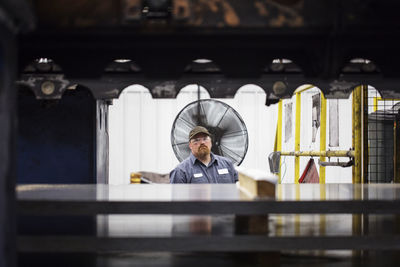 Portrait of worker standing against metal sheets in steel industry factory