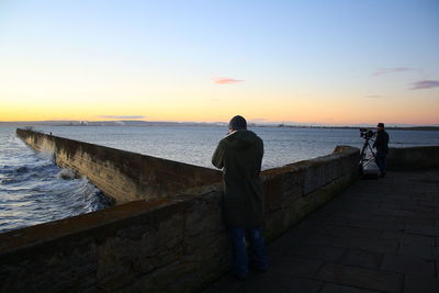 Men standing by sea during sunset