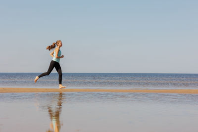 Rear view of woman standing at beach against clear sky