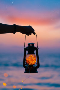 Silhouette person photographing illuminated lamp against sky during sunset