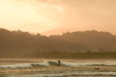 Man surfing on sea against sky during sunset