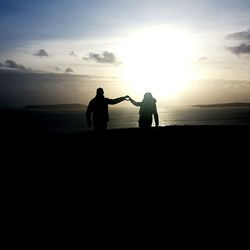 Silhouette men standing on beach against sky during sunset