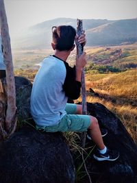 Man sitting on field against mountain