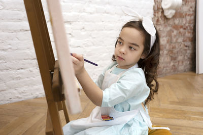 Cute girl drawing on white sheet on a drawing easel. little painting artist.