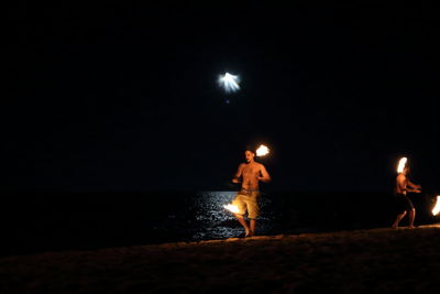 People standing on beach against sky at night