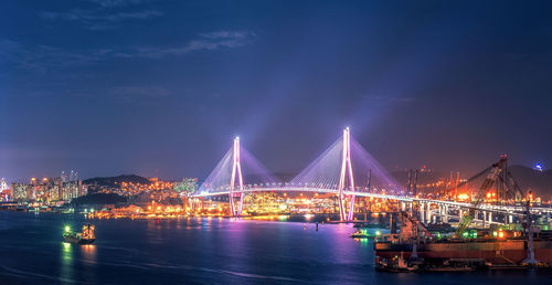 Illuminated bridge over river in city at night