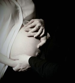 Cropped image of husband touching his pregnant wife belly in darkroom