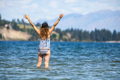 Rear view of woman with arms raised in lake