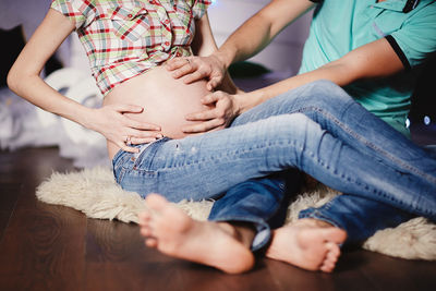 Midsection of pregnant woman and man sitting with hands on stomach