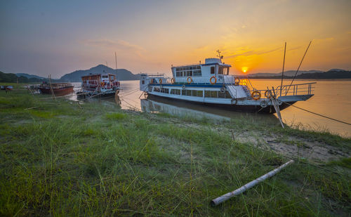 Boat moored on shore by sea against sky during sunset