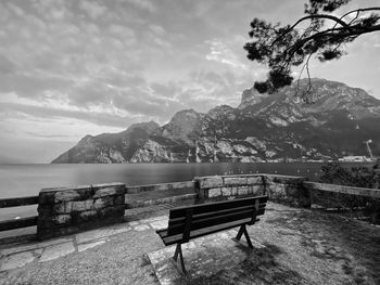 Empty bench by lake against sky