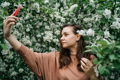 Portrait of young woman with arms raised against plants