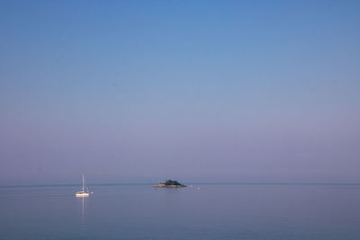 Sailboat in sea and small island against clear sky