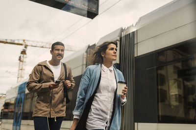 Low angle view of man and woman walking by tram at station