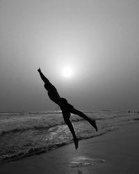 Silhouette man with arms raised on beach against sky