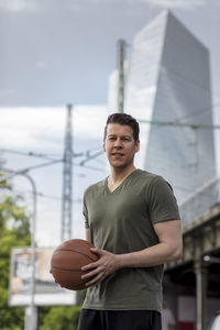 Portrait of young man with basketball standing outdoors