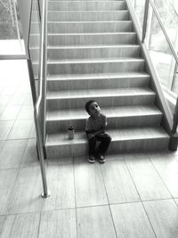 High angle view of cute boy sitting by coffee cup on steps