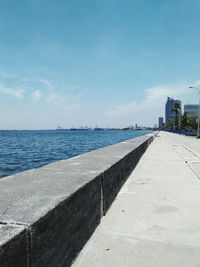 Footpath by sea against sky in city