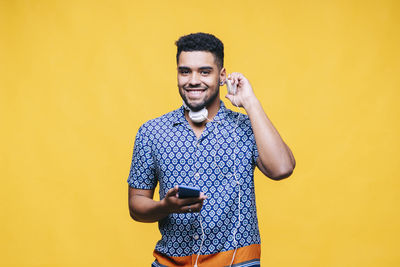 Portrait of smiling young man using mobile phone against yellow wall
